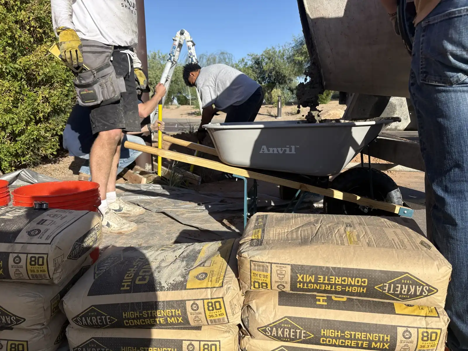 Installation crew preparing concrete for shade sail post footings on site