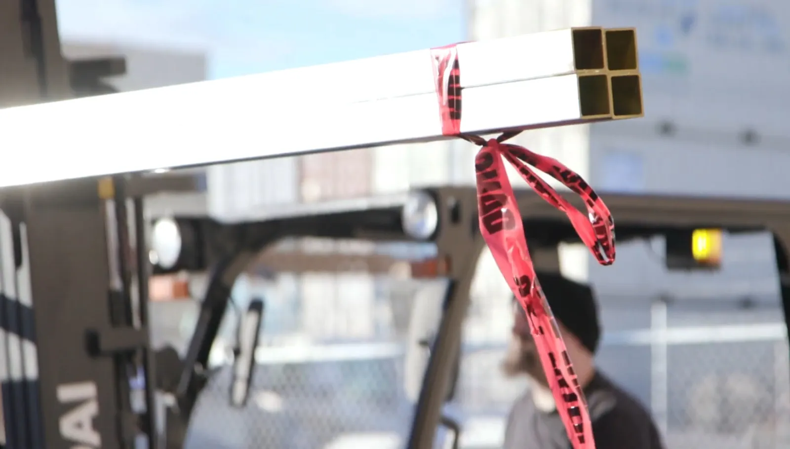 Powder-coated square steel post staged for fabrication, tagged with caution ribbon
