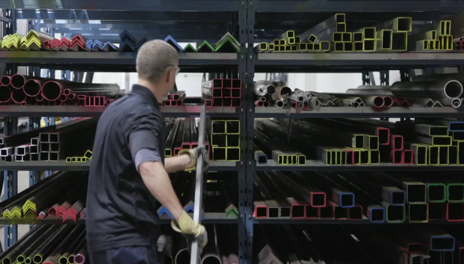 Worker pulling steel tubing from a stocked supply rack