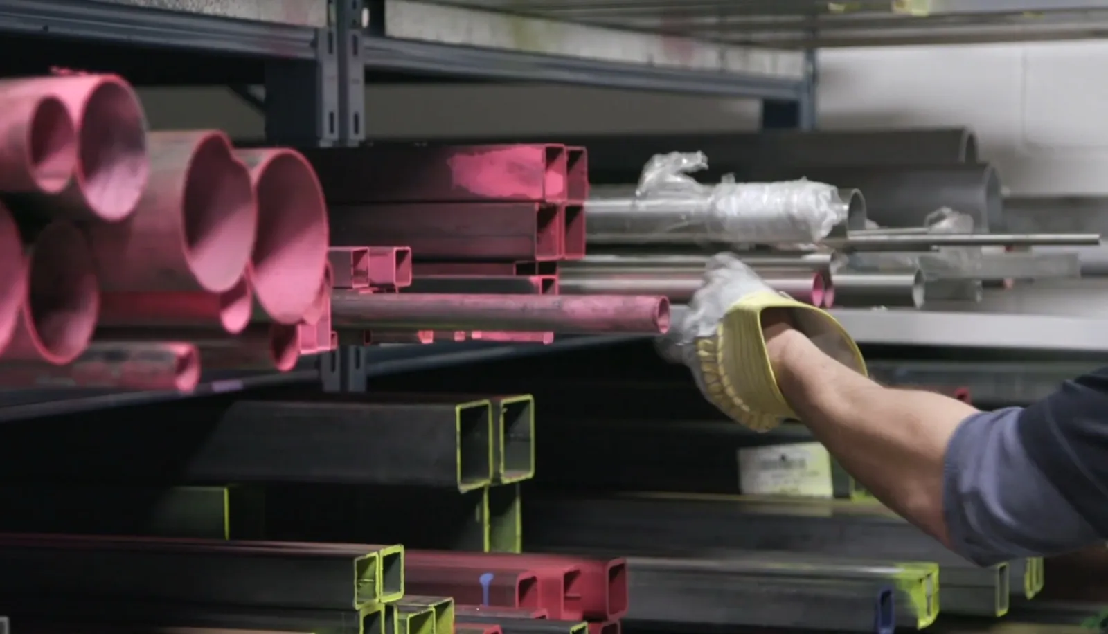 Gloved hand selecting a length of steel tube from a supply rack