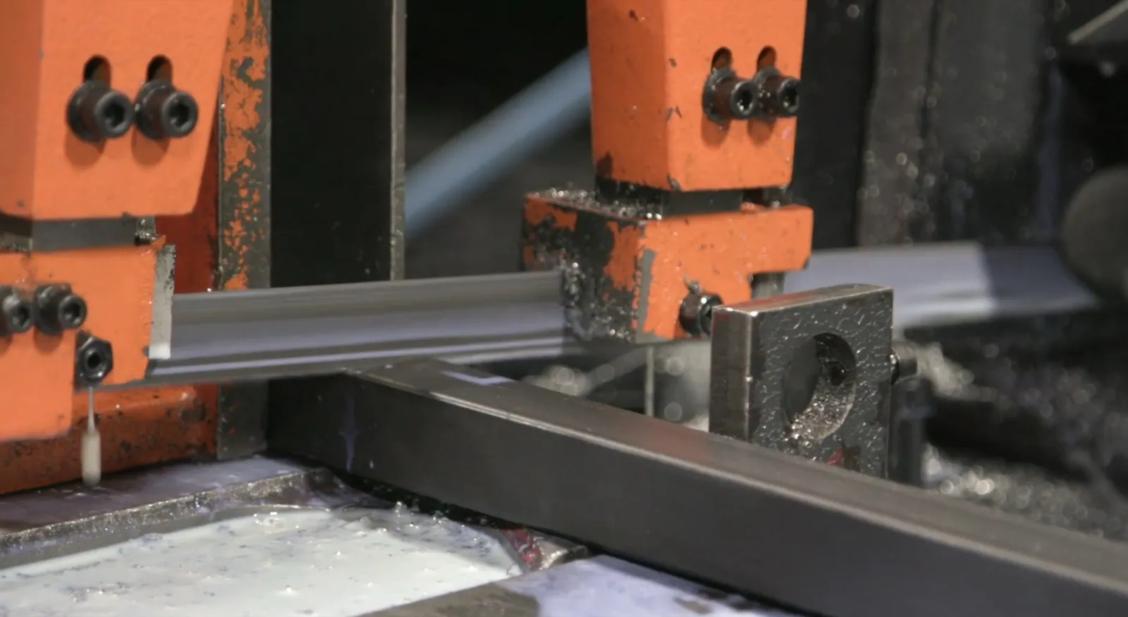 Structural steel stock being cut on a band saw with coolant